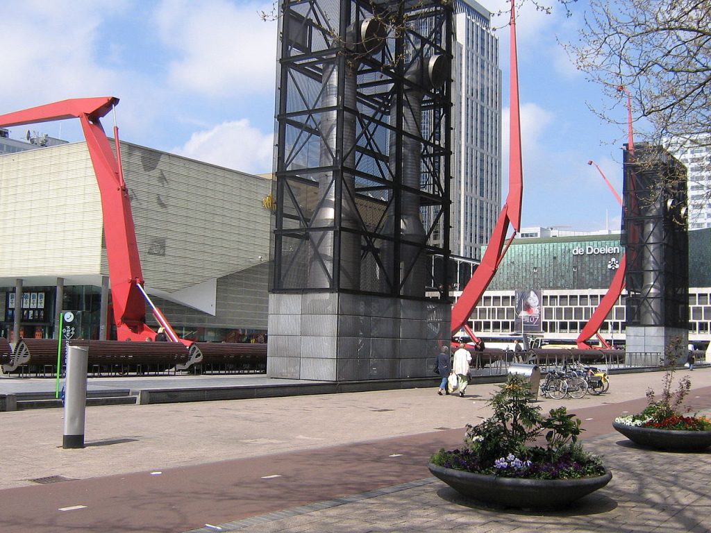 Openluchtbioscoop op het Schouwburgplein in Rotterdam met films op groot scherm onder de sterrenhemel, omringd door karakteristieke architectuur.